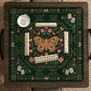 May include: A dark green Mahjong mat featuring a central moth illustration surrounded by floral patterns and butterflies. The mat includes printed game instructions, four wooden tile racks, and a small white bowl containing Mahjong tiles.