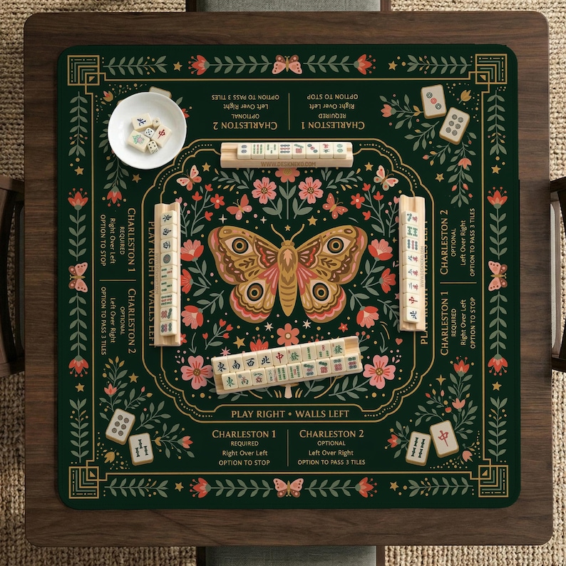 May include: A dark green Mahjong mat featuring a central moth illustration surrounded by floral patterns and butterflies. The mat includes printed game instructions, four wooden tile racks, and a small white bowl containing Mahjong tiles.