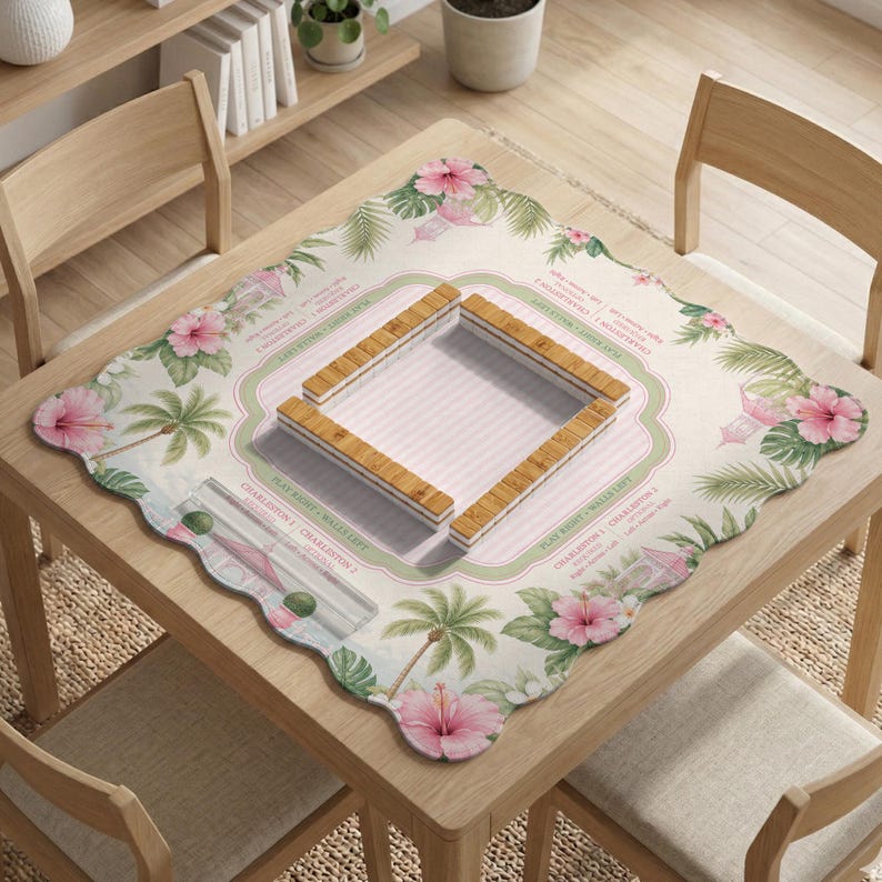 May include: A square mahjong mat with a scalloped edge featuring a tropical print of pink hibiscus flowers and palm trees. The center has a light pink striped square with four wooden mahjong tile racks arranged in a square formation.