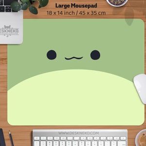 May include: A large mousepad with a cartoon frog face design. The mousepad is light green and yellow with black eyes and a curved mouth. It measures 18 x 14 inches. The website address www.deskneko.com is printed at the bottom.