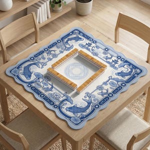 May include: A square mahjong mat with a scalloped edge featuring a blue and white pattern of koi fish, lotus flowers, and pagodas. In the center, four wooden mahjong racks are arranged in a square formation on a white surface with a circular design.