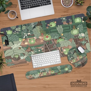 Puede incluir: Una configuración de escritorio con una alfombrilla de ratón rectangular grande, una alfombrilla de ratón redonda y un reposamuñecas, todos con un patrón repetido de ranas de dibujos animados en un invernadero. También hay un teclado y un ratón.