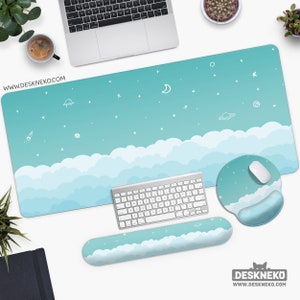 May include: A desk setup with a light blue desk mat featuring a cloud and space design. Includes a matching mousepad, wrist rest, and a white keyboard. The website address www.deskneko.com is visible.