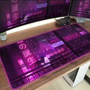 Op de afbeelding: Een rechthoekige muismat met een neonpaars stadsgezichtontwerp. De mat heeft Japanse tekst en een silhouet van een kat. De woorden "KAWAII" en "DESKNEKO.COM" zijn ook zichtbaar. De mat heeft een gloeiende paarse rand.