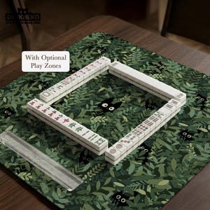 May include: A Mahjong set arranged on a green play mat with a leaf and black cat design. The white tiles are arranged in a square, with red and green characters. The text "With Optional Play Zones" is visible.
