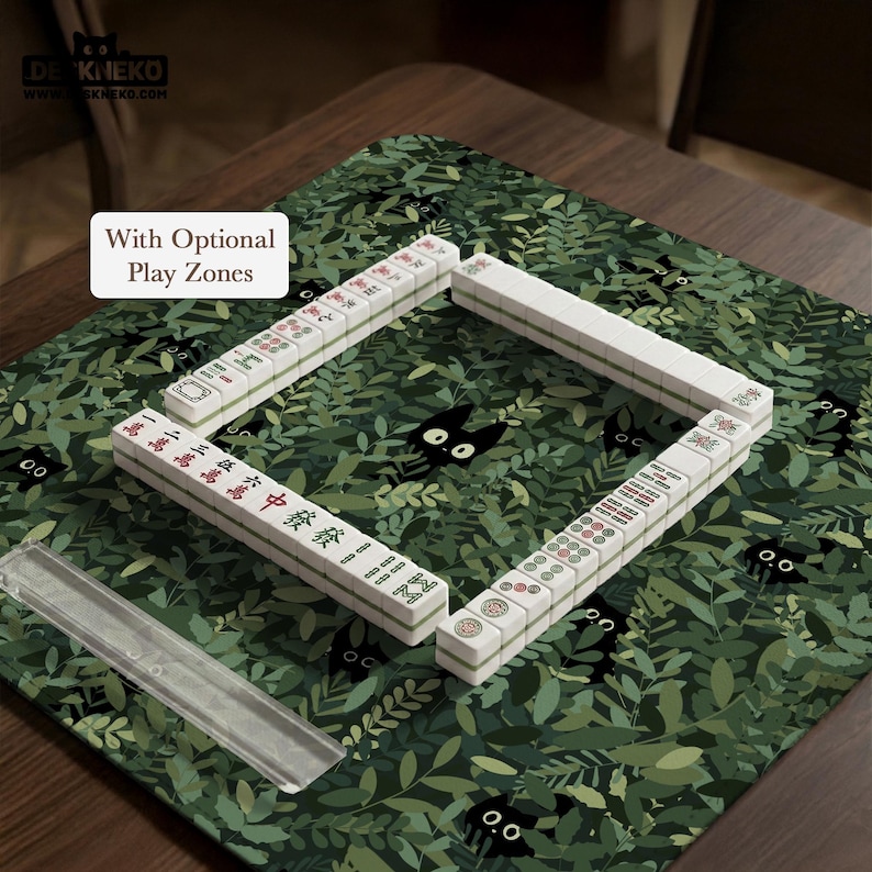 May include: A Mahjong set arranged on a green play mat with a leaf and black cat design. The white tiles are arranged in a square, with red and green characters. The text "With Optional Play Zones" is visible.