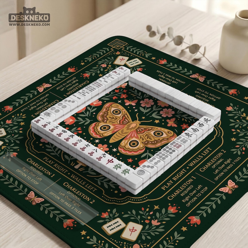 May include: A square dark green mahjong mat featuring a central moth illustration surrounded by floral motifs and butterflies. The mat includes printed text detailing Charleston rules and wall directions, with white mahjong tiles arranged in a square.