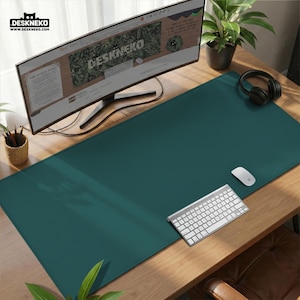 Op de afbeelding: Een teal bureaumat met een computermonitor, toetsenbord, muis en koptelefoon op een houten bureau. De monitor toont de website "DESKNEKO". Een kleine plant en een potloodhouder zijn ook zichtbaar.