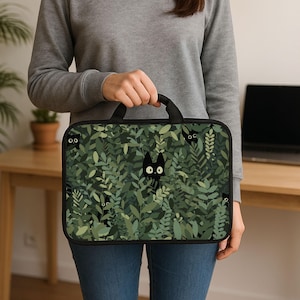 Może przedstawiać: Czarna torba na laptopa z fantazyjnym wzorem czarnych kotów wyglądających z gęstego, zielonego wzoru liści. Torba ma czarny uchwyt i czarną obwódkę, oferując stylowe i ochronne akcesorium do laptopów.