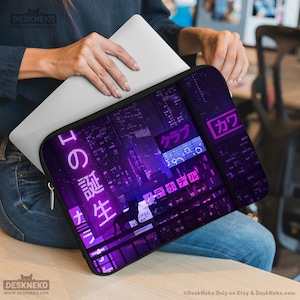 Puede incluir: Una funda negra para portátil con un diseño de paisaje urbano púrpura, texto japonés y una silueta de gato. La funda está abierta, revelando un portátil plateado. El diseño incluye letreros de neón y luces de edificios.