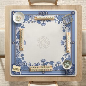 May include: A square mahjong table with a blue and white floral design. The table is set with tiles, dice, and small bowls. The table has a wooden frame and is set on a light-colored rug. The logo "DESKNEKO" is visible.