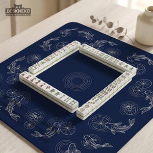 K&ouml;nnte beinhalten: Eine dunkelblaue, quadratische Mahjong-Matte mit einem wei&szlig;en Linienmuster aus Koi-Fischen und Lotusblumen. In der Mitte befindet sich eine rechteckige Anordnung wei&szlig;er Mahjong-Steine mit verschiedenen roten, gr&uuml;nen und schwarzen Gravuren.