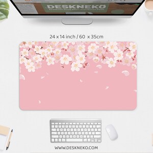 May include: A rectangular desk mat with a pink background and a floral design of white and light pink cherry blossoms along the top edge. The mat measures 24 x 14 inches.