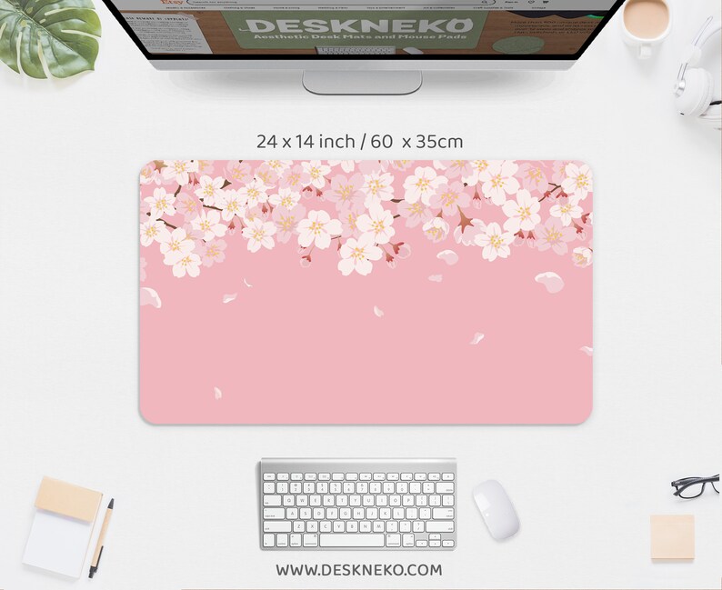 May include: A rectangular desk mat with a pink background and a floral design of white and light pink cherry blossoms along the top edge. The mat measures 24 x 14 inches.