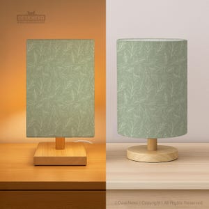 Könnte beinhalten: Zwei Lampen mit hellgrünen Lampenschirmen mit weißem Blättermuster. Die Lampen haben einen Holzsockel und einen zylindrischen oder rechteckigen Schirm. Der Text "Deskneko" ist sichtbar.