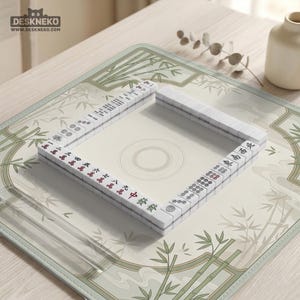 May include: A square mahjong mat featuring a light green and cream bamboo pattern with a central circular design. White mahjong tiles with red, green, and black characters and symbols are arranged in a square formation on the mat surface.