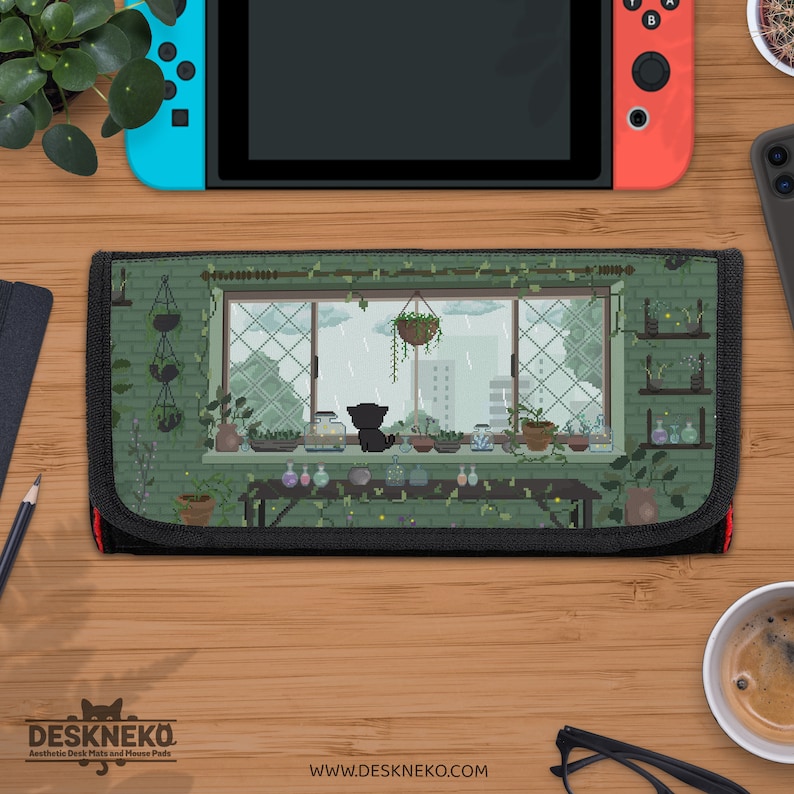 May include: A black and green Nintendo Switch case with a pixelated illustration of a cat gazing out of a window at a rainy scene. The window is framed by plants and pots. The case has a black border and the text "DESKNEKO" and "www.deskneko.com".