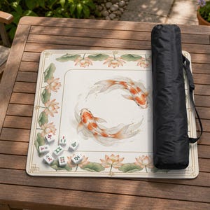 May include: A beige Mahjong game mat with a koi fish design and lotus flower accents. Includes a black carrying case and several white tiles with Chinese characters. The mat is rectangular and has a decorative border.