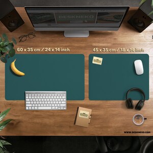 Op de afbeelding: Twee teal bureaumatten, &eacute;&eacute;n van 60 x 35 cm en de andere van 45 x 35 cm, liggen op een houten bureau. Een toetsenbord, banaan, notitieblok, muis, koptelefoon en koffiekopje staan ook op het bureau. De website is zichtbaar.