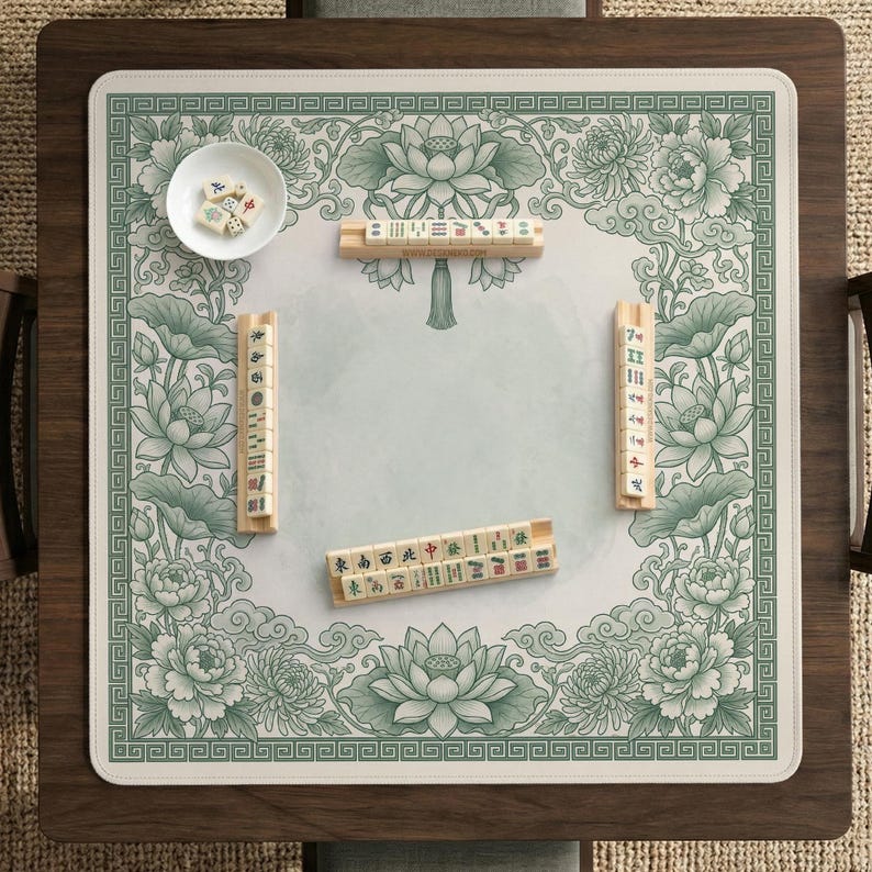 Puede incluir: Una mesa de juego de Mahjong cuadrada con un dise&ntilde;o floral verde y blanco. La mesa presenta un marco de madera y una superficie de juego con motivos de loto y peon&iacute;as. Varias fichas de Mahjong y un peque&ntilde;o cuenco con dados est&aacute;n dispuestos sobre la mesa.