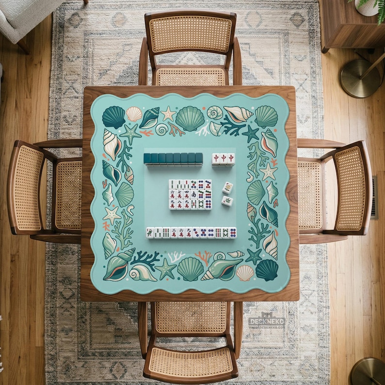 May include: A square wooden mahjong table with a light blue mat featuring a seashell design. The table is surrounded by four wooden chairs with woven backs. Mahjong tiles are arranged on the mat, ready for play.