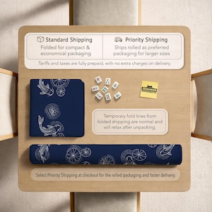 Puede incluir: Una alfombrilla de escritorio azul marino con un dise&ntilde;o de peces koi y nen&uacute;fares blancos, tanto plegada como enrollada. La imagen tambi&eacute;n muestra fichas de mahjong y una pegatina "DESKNEKO" sobre una superficie de madera.