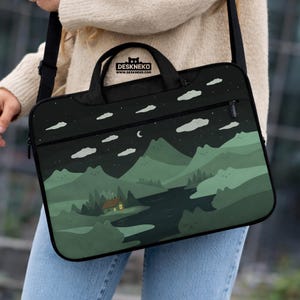 May include: Black laptop bag with a scenic landscape design. The design features a night sky with clouds, stars, and a crescent moon over green mountains, a river, and a cabin with a lit window. The bag has a handle and a shoulder strap. The brand name "DESKNEKO" is printed on the top.