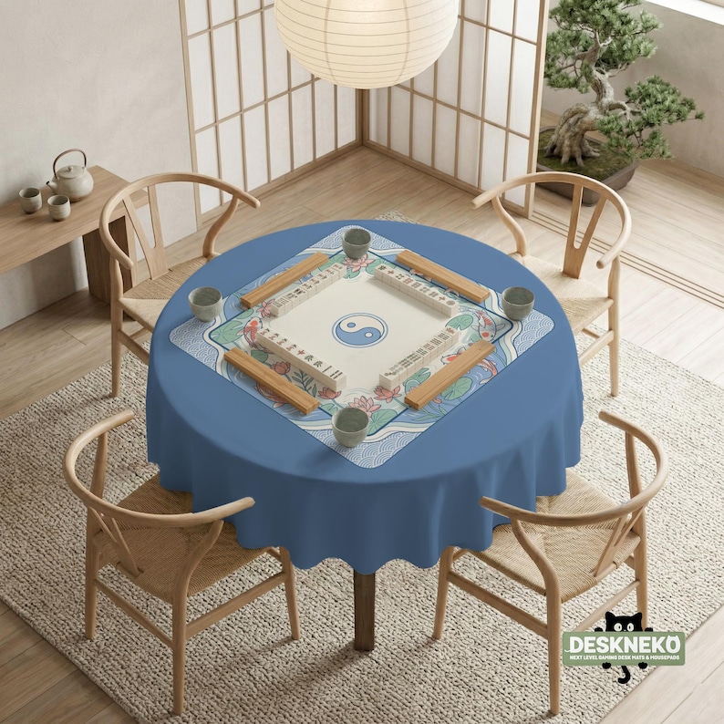 May include: A circular blue table set for Mahjong, with four wooden chairs around it. The table has a Mahjong mat with a Yin Yang symbol and floral designs. A paper lantern hangs above, with a bonsai tree and tea set in the background.