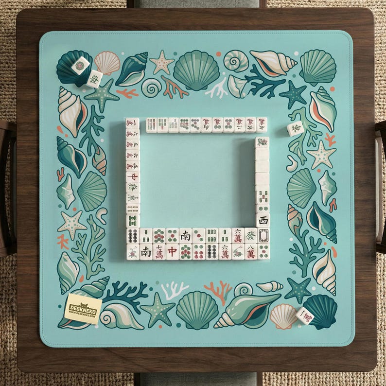 May include: A square Mahjong game mat in light blue, decorated with seashell and coral designs. The mat has a central playing area framed by a border of illustrations. Mahjong tiles are arranged on the mat, ready for play.