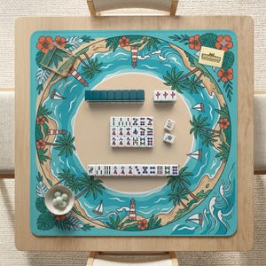 May include: A mahjong game set on a wooden table. The game board has a tropical island design with palm trees, sailboats, and a lighthouse. The set includes tiles in various colours and designs, along with a set of green dice.