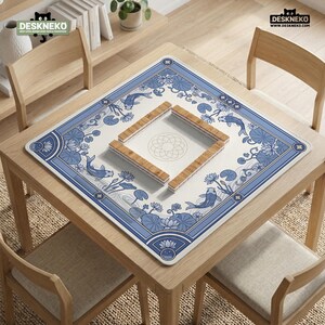 May include: A square table mat with a blue and white koi fish and floral design. The mat is centered on a light wood table, with four wooden chairs around it. The mat has a square cutout in the center with wooden pieces.