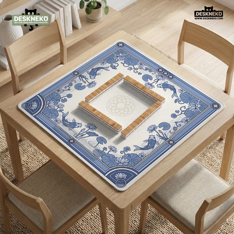May include: A square table mat with a blue and white koi fish and floral design. The mat is centered on a light wood table, with four wooden chairs around it. The mat has a square cutout in the center with wooden pieces.