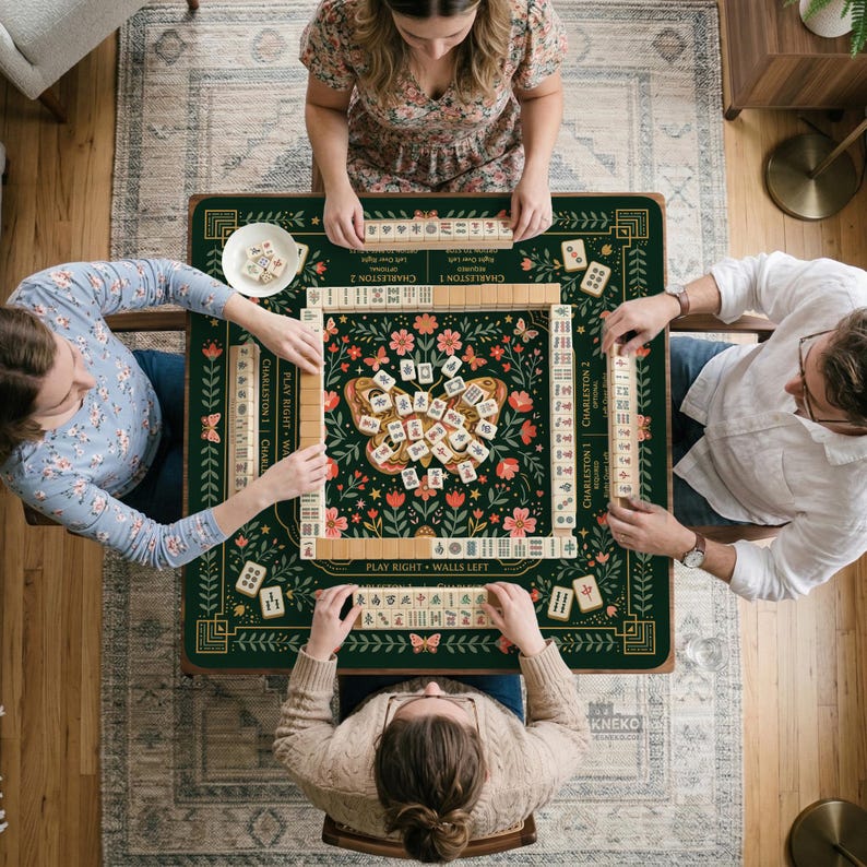 May include: A square mahjong game mat featuring a dark green background with a central butterfly illustration, floral motifs, and gold-colored border lines. The mat displays game text including Charleston 1, Charleston 2, and Play Right Walls Left.
