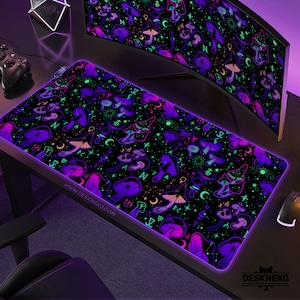May include: A black desk mat with a repeating pattern of purple and teal mushrooms, moons, and stars. The mat has a glowing purple border and the website address www.deskneko.com printed on it. A computer monitor and other accessories are visible in the background.