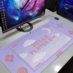 K&ouml;nnte beinhalten: Ein lila Gaming-Mauspad mit Pastell-Design. Das Pad zeigt den Text "HELLO PLAYER ONE" mit Wolken, Sternen und einem Mond. Es hat ein vom Controller inspiriertes Design mit rosa Akzenten und dem Text "LEVEL 1".