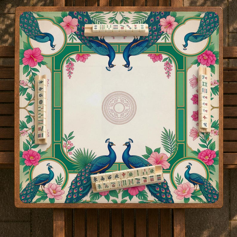 May include: A square mahjong table featuring a cream-colored surface with a decorative border of blue peacocks, green foliage, and pink hibiscus flowers. Four wooden tile racks are positioned on the edges, each holding a row of ivory-colored mahjong tiles.