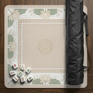 May include: A beige Mahjong game mat with a floral design and a black carrying case. The mat features lotus flowers and a geometric pattern. Several Mahjong tiles are scattered on the mat.
