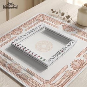 May include: A Mahjong set with white tiles and red and green markings is arranged on a decorative mat. The mat features a light pink and white floral design with a geometric center. The logo "DESKNEKO" is visible in the top left corner.