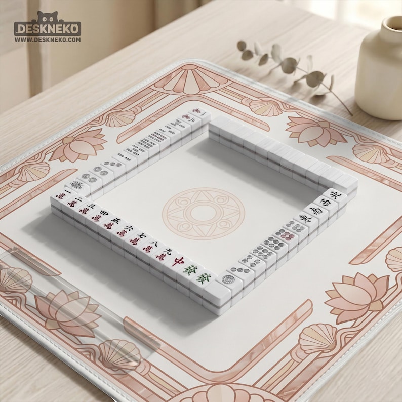May include: A Mahjong set with white tiles and red and green markings is arranged on a decorative mat. The mat features a light pink and white floral design with a geometric center. The logo "DESKNEKO" is visible in the top left corner.