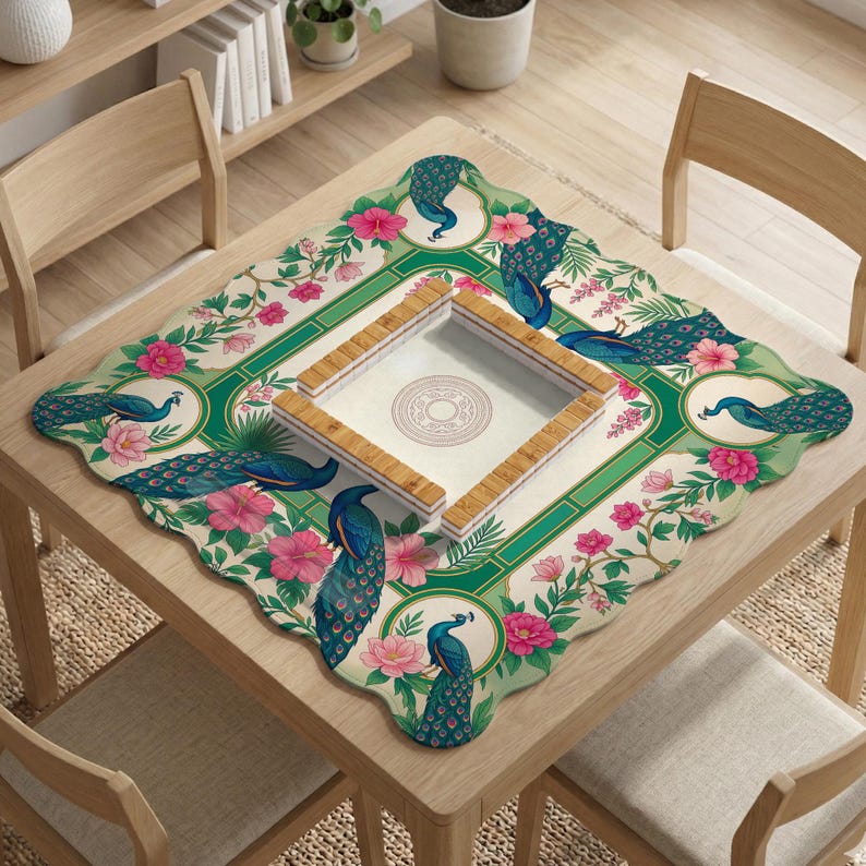 May include: A square mahjong table mat featuring a cream-colored background with a green border, decorated with blue peacock illustrations and pink hibiscus flowers. A wooden mahjong tile rack frame sits in the center of the mat.