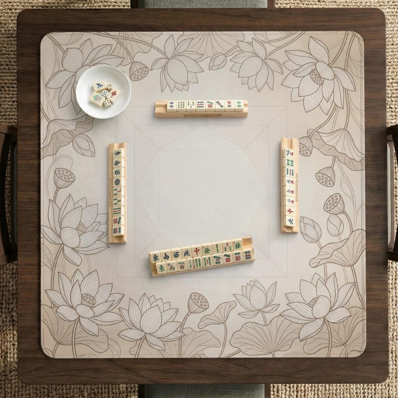 Puede incluir: Una mesa de Mahjong de madera con una esterilla beige con estampado floral con flores de loto. La mesa tiene un marco de madera marr&oacute;n oscuro y contiene varios juegos de fichas de Mahjong y un cuenco blanco peque&ntilde;o con dados.