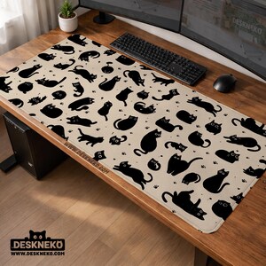 May include: A beige desk mat with a repeating pattern of black cat silhouettes and paw prints. The mat has rounded corners and the text "WWW.DESKNEKO.COM" along the bottom edge. The mat is designed to protect a desk surface.