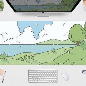May include: A long rectangular mouse pad featuring a cartoon landscape with a blue lake, green hills, and fluffy white clouds under a blue sky. The design includes trees and a small animal figure. The pad is on a white desk with a keyboard and mouse.