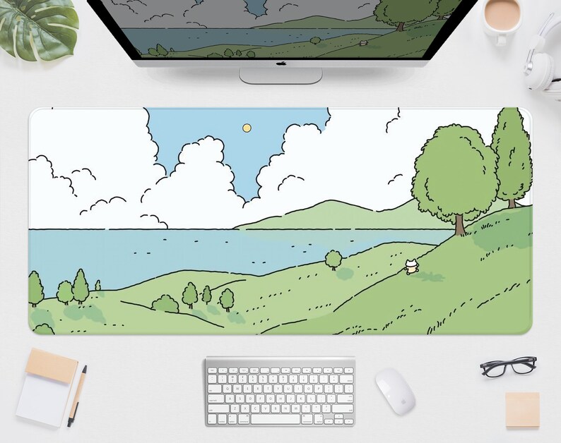 May include: A long rectangular mouse pad featuring a cartoon landscape with a blue lake, green hills, and fluffy white clouds under a blue sky. The design includes trees and a small animal figure. The pad is on a white desk with a keyboard and mouse.