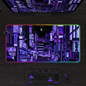 May include: A rectangular gaming mousepad with a pixelated cityscape design in shades of purple and blue, with the word "TOKYO" visible. The mousepad has a glowing, multi-colored edge. A keyboard, mouse, and headset are also visible.