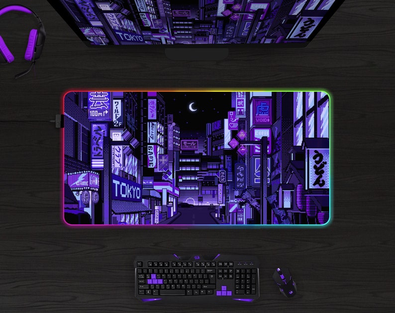 May include: A rectangular gaming mousepad with a pixelated cityscape design in shades of purple and blue, with the word "TOKYO" visible. The mousepad has a glowing, multi-colored edge. A keyboard, mouse, and headset are also visible.