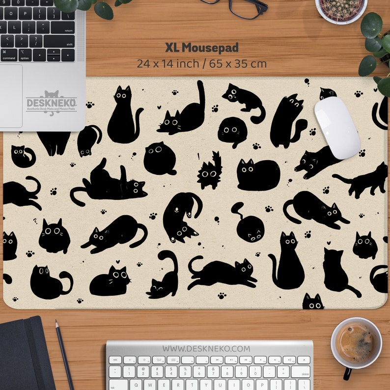 Puede incluir: Alfombrilla de rat&oacute;n XL con un fondo beige y un patr&oacute;n de ilustraciones de gatos negros en varias poses. La alfombrilla mide 65 x 35 cm. El texto "XL Mousepad" est&aacute; impreso en la parte superior.
