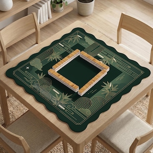 Pode incluir: Um tapete de Mahjong verde com borda ondulada, com desenhos dourados de bambu e nuvens. O tapete est&aacute; sobre uma mesa de madeira com um quadrado de pe&ccedil;as de Mahjong. A cena &eacute; iluminada por luz natural.