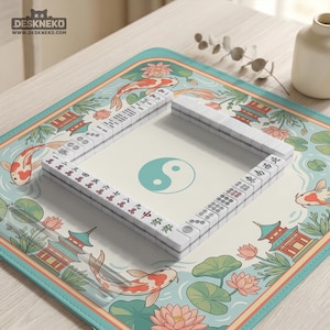 May include: A complete Mahjong set with white tiles and red and black characters, arranged on a decorative mat. The mat features a koi fish, lotus flowers, and pagodas in a teal and cream color scheme. The Yin and Yang symbol is in the center.