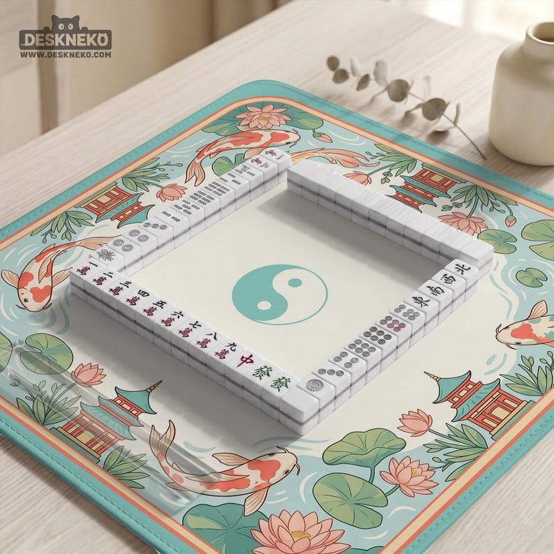May include: A complete Mahjong set with white tiles and red and black characters, arranged on a decorative mat. The mat features a koi fish, lotus flowers, and pagodas in a teal and cream color scheme. The Yin and Yang symbol is in the center.